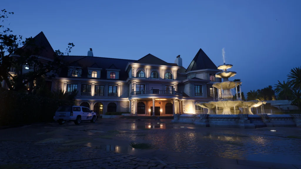The front of a lit luxurious house with a fountain on the right in one of the DLCs of Ready or Not